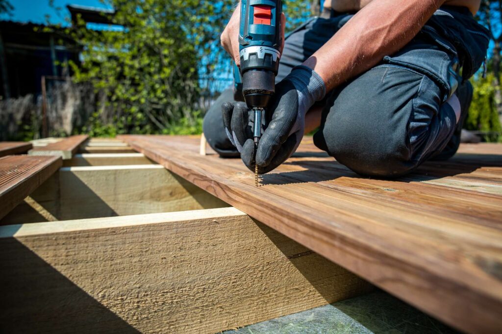 nz Deck construction, builder hand with electric screwdriver installing impregnated wooden boards