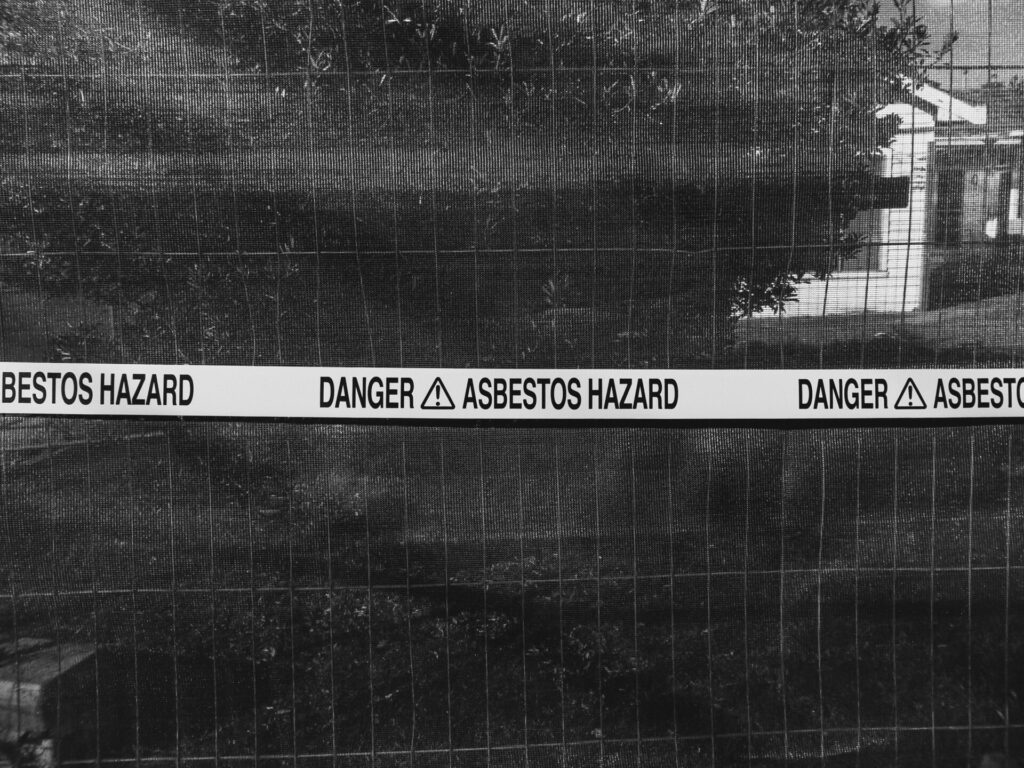 Black and white photo of an asbestos hazard warning sign on a fence.