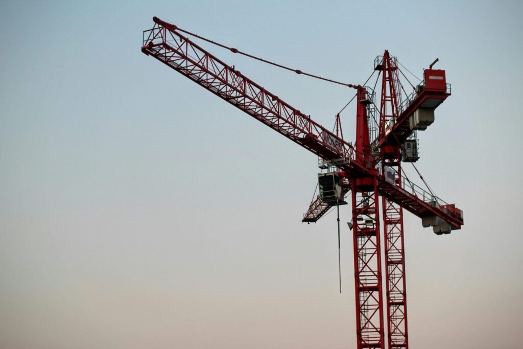 A red tower crane on a construction site set against a clear sky during daytime.