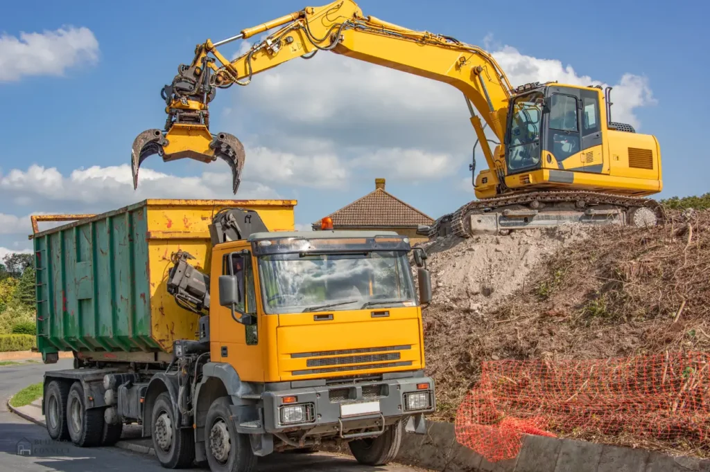 Excavator with grab attachment loading debris into a dump truck during demolition in New Zealand