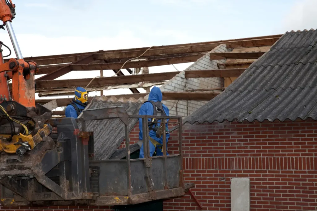 Workers in protective gear removing asbestos roofing sheets during demolition in New Zealand.