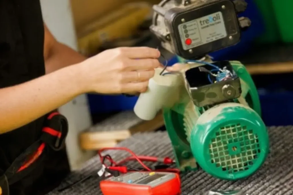Technician repairing a small green electric water pump installed in New Zealand.