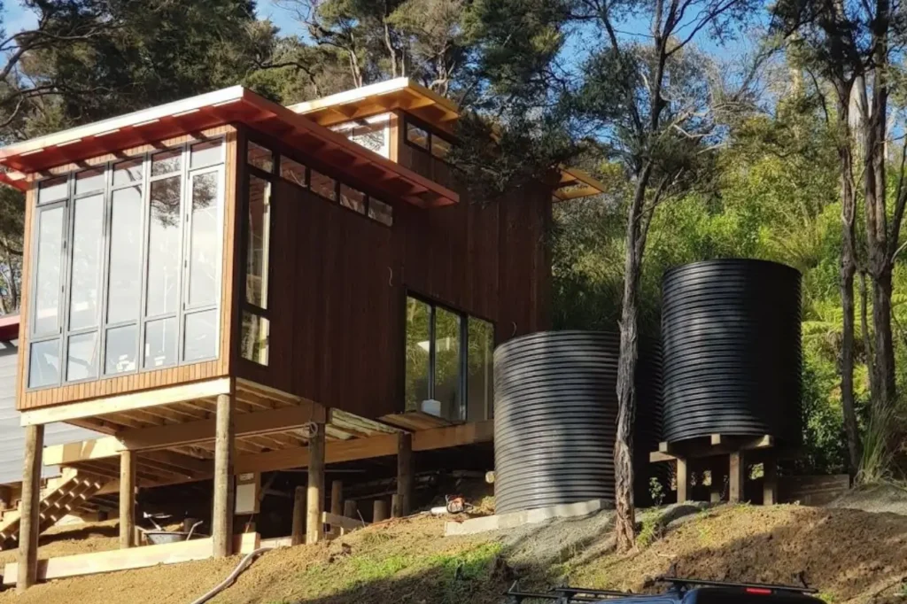 Black water tanks beside a wooden rural home showing Water Tank Installation in New Zealand NZ.