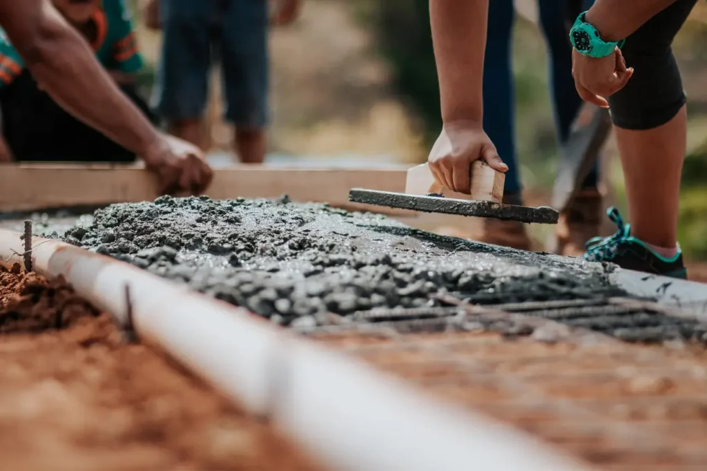 Workers pouring and levelling fresh concrete over reinforcement mesh during foundation construction by Foundation Contractors New Zealand.