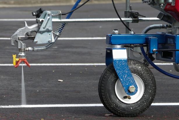 Line marking machine applying fresh paint to asphalt surface in New Zealand car park.