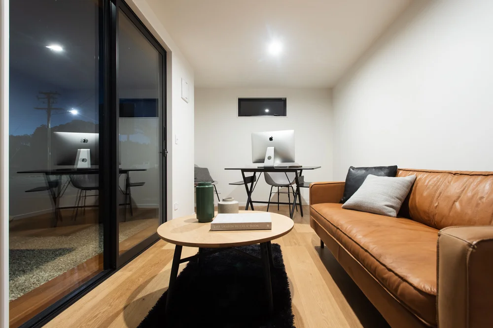 At Tiny Homes New Zealand a stylish compact interior featuring a leather sofa round coffee table and dual workspace setup with sleek desktop computers