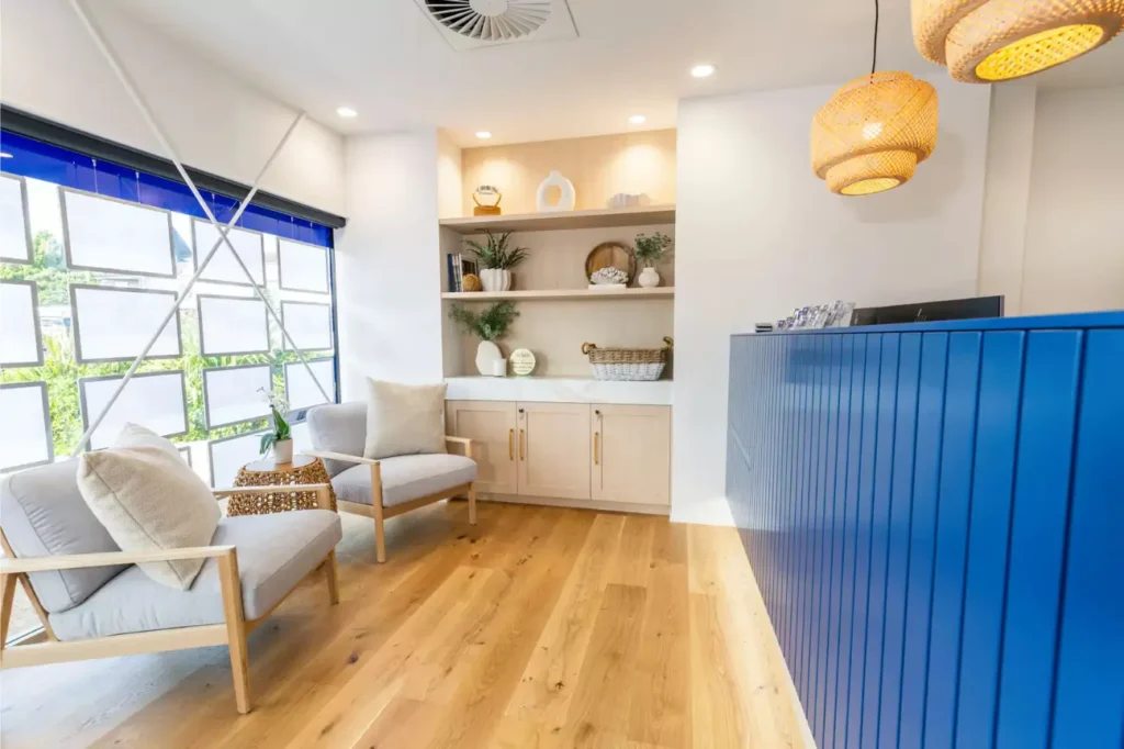 Modern office reception lounge with timber flooring, custom shelving, and blue reception desk in an Office Fit Outs New Zealand project.