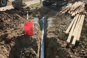 Expert drain layers in New Zealand installing a new PVC drainage pipe within a precisely excavated trench on a construction site.