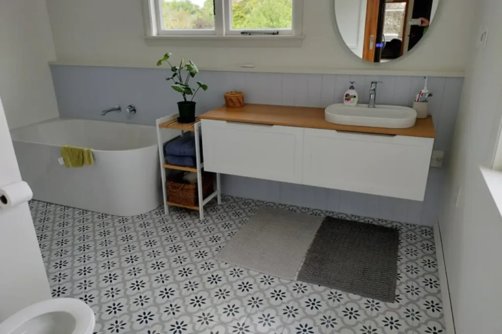 Skilled Tiler in New Zealand fitting patterned bathroom floor tiles and wall tiles in a bright renovated space.