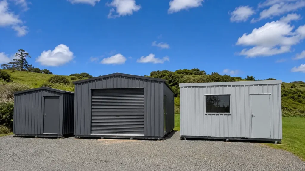 Three transportable units representing various custom cabin builds Auckland styles standing side by side on a gravel lot under a blue sky.